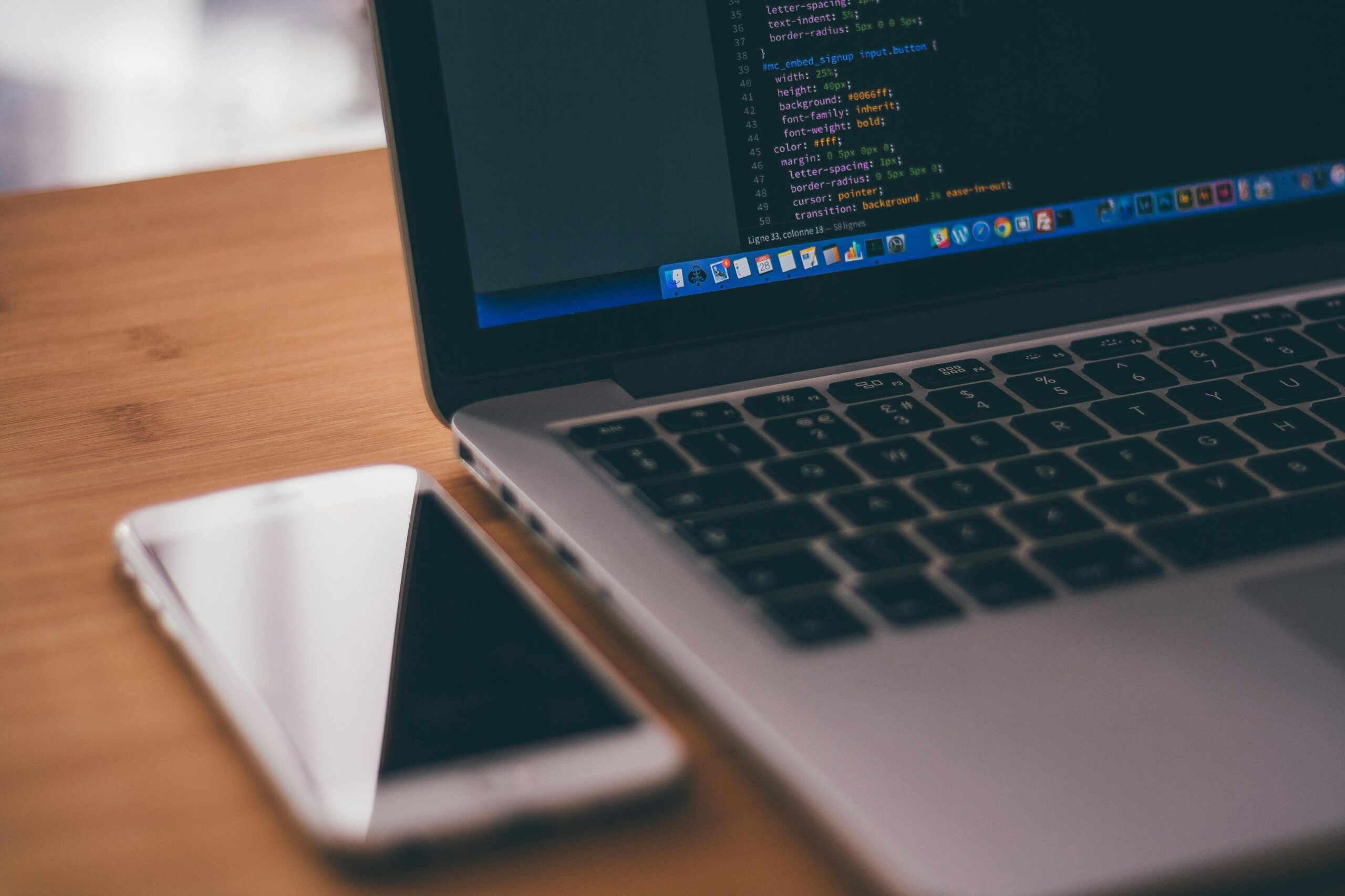 Coding setup with laptop displaying code and smartphone on a wooden table, ideal for tech themes.